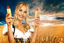 Young Sexy Oktoberfest Girl Waitress, Wearing A Traditional Bavarian Or German Dirndl With Two French Hot Dogs Outdoor.