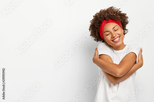 Fotografía Horizontal shot of pleasant looking African American woman hugs herself, remembe
