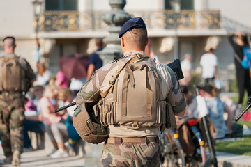 An unidentified Man in military uniform and with a military weapon patrolling the streets of the city during a public event.