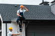 © LIGHTFIELD STUDIOS - handsome repairman sitting on roof and holding toolbox near coworker in helmet