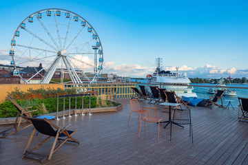 Wall Mural - Hlsinki. Finland. Harbor for tourists. Ferris Wheel in Helsinki. Motor ship at the pier. Street chairs on a city pier. Ferris wheel on the promenade. Sea travel to Finland. Travels on the ship