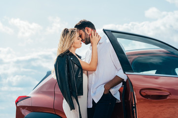 Wall Mural - attractive woman and handsome man kissing and hugging near car