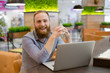 © ruslanshug - happy laughing young handsome bearded trendy man sitting with silver laptop in cafe during coffee break
