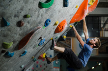 Strong Healthy Sport Caucasian Man With Beard And Eyeglasses Climbing On Wall Indoors During Bouldering Exercise