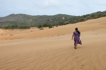 A Wayúu woman in traditional outfit walking in sand dunes in the desert. La Macuira, La Guajira, Colombia