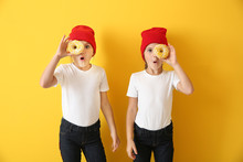 Portrait Of Surprised Twin Girls With Tasty Donuts On Color Background