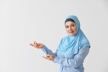 Wall Mural - Beautiful mature Muslim woman showing something on light background