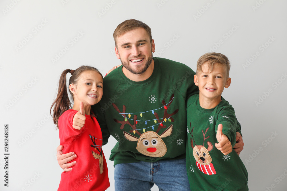 Happy man and his children in Christmas sweaters on light background
