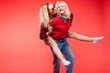 © Вячеслав Косько - Stock studio portrait of two cheerful and positive trendy girlfriends or sisters having fun. Girl in sunglasses making bunny ears to her friend with her hand while sitting on her back. Isolate on red.