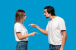 © ianachyrva - Couple of a young blond woman and brunet bearded man with mustaches in white t-shirts and blue jeans quarreling standing isolated over blue background. Concept of relationship crisis.