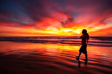 Wall Mural - woman walking alone on the beach in the sunset