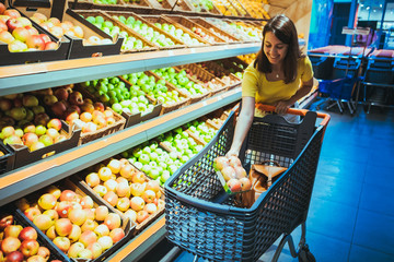 Wall Mural - young pretty adult woman do shopping in grocery store buying apple