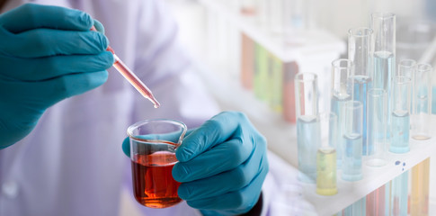 Wall Mural - laboratory research concept; scientist dropping chemical reagent into beaker with lab glassware back