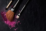 Make-up brushes with crushed cosmetics, shot from above on a black background with copyspace, a beauty design template for a makeup banner