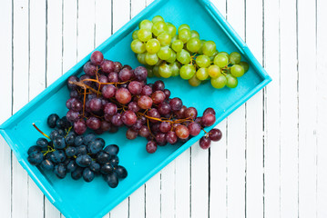 Wall Mural - red and white grapes variation on blue tray, white wooden table background