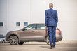 © flowertiare - Middle-aged  tall gray-haired businessman in blue suit with brown briefcase walks to his car on the private parking