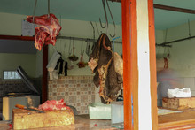 Beef And Stomach On Iron Hooks In Simple Shop Near Road On Java Island. Traditional Butcher Shop With Beef At Muslim Vendors In Indonesia. Meat Shop On The Street. Wooden Cutting Board With Chisel.