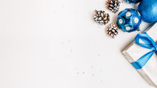 Winter Holidays. Cropped Flat Lay Of Silver Gift Box, Blue Baubles And Pine Cones On White Background. Copy Space.