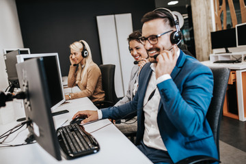 Wall Mural - Handsome male customer service agent with headset working in call center.