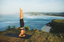 Woman Practicing Yoga And Making Handstand Pose Outdoor With Amazing Ocean View. Health And Fitness Concept. Nature Background.