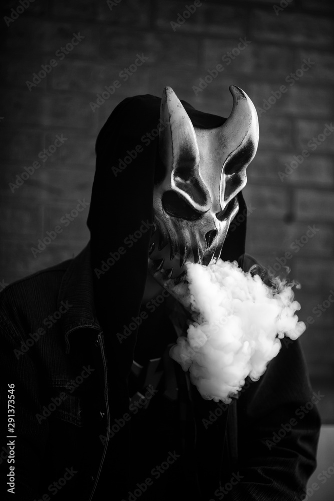 Photo Stock Vape man in devil mask and a hood smoking an electronic  cigarette indoors. Puffs of steam. Bad habit that is harmful to health.  Vaping activity. Black and white. | Adobe