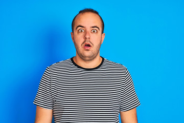 Sticker - Young man wearing striped navy t-shirt standing over isolated blue background afraid and shocked with surprise expression, fear and excited face.