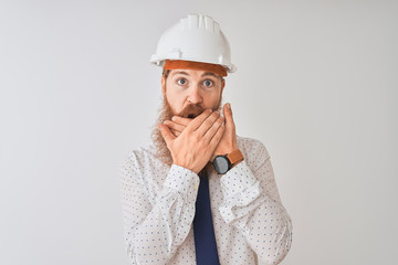 Canvas Print - Young redhead irish architect man wearing security helmet over isolated white background shocked covering mouth with hands for mistake. Secret concept.