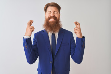 Sticker - Young redhead irish businessman wearing suit standing over isolated white background gesturing finger crossed smiling with hope and eyes closed. Luck and superstitious concept.