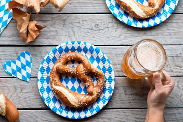 Wall Mural - Oktoberfest traditional food and beer. Hand holding beer mug, pretzels on paper plates