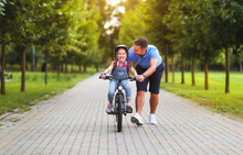 Happy Family Father Teaches Child Daughter To Ride A Bike In The Park  .