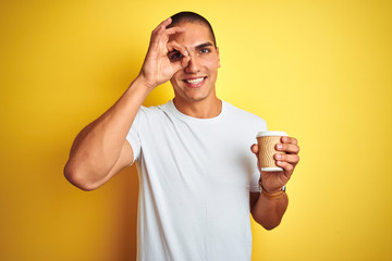 Poster - Young handsome man drinking a take away glass of coffee over yellow isolated background with happy face smiling doing ok sign with hand on eye looking through fingers