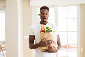 Sticker - African american man holding paper bag full of fresh groceries scared in shock with a surprise face, afraid and excited with fear expression