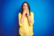 © Krakenimages.com - Young beautiful woman wearing yellow t-shirt standing over blue isolated background shocked covering mouth with hands for mistake. Secret concept.