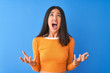 Young beautiful chinese woman wearing orange t-shirt standing over isolated blue background crazy and mad shouting and yelling with aggressive expression and arms raised. Frustration concept.