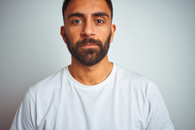 Young Indian Man Wearing T-shirt Standing Over Isolated White Background With Serious Expression On Face. Simple And Natural Looking At The Camera.
