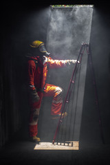 Noise and grain defocus of firefighter man in safety fire suit and oxygen tank on rescue duty climbing a ladder out of burning premises. Fireman into burning building area with smoke.