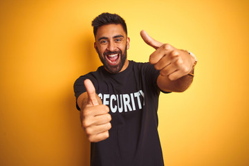 Arab indian hispanic safeguard man wearing security uniform over isolated yellow background approving doing positive gesture with hand, thumbs up smiling and happy for success. Winner gesture.