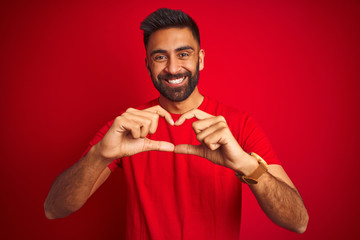 Wall Mural - Young handsome indian man wearing t-shirt over isolated red background smiling in love showing heart symbol and shape with hands. Romantic concept.