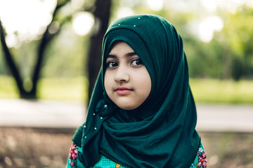 Wall Mural - Portrait of happy little muslim girls child with hijab dress smiling and looking at camera in the park