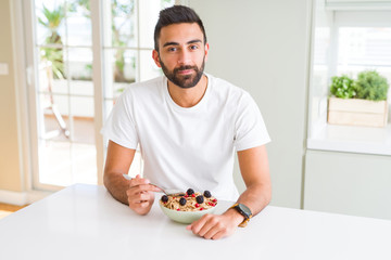 Poster - Handsome hispanic man eating healthy breakfast in the morning at home with a confident expression on smart face thinking serious