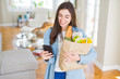 © Krakenimages.com - Young woman holding a paper bag full of fresh groceries and using smartphone app for supermarket delivery