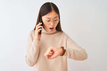 Poster - Young chinese woman talking on the smartphone over isolated white background Looking at the watch time worried, afraid of getting late