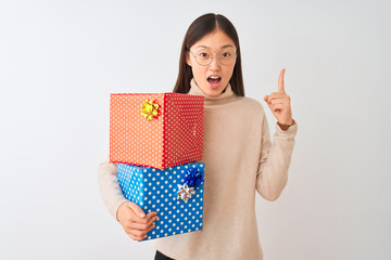 Sticker - Young chinese woman holding birthday gifts over isolated white background pointing finger up with successful idea. Exited and happy. Number one.