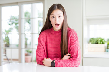 Poster - Beautiful Asian woman wearing pink sweater on white table afraid and shocked with surprise expression, fear and excited face.