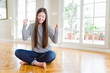 © Krakenimages.com - Beautiful Asian woman sitting barefoot on the floor at home very happy and excited doing winner gesture with arms raised, smiling and screaming for success. Celebration concept.