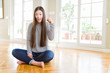 © Krakenimages.com - Beautiful Asian woman sitting barefoot on the floor at home pointing finger up with successful idea. Exited and happy. Number one.
