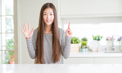 Poster - Beautiful Asian woman wearing stripes sweater showing and pointing up with fingers number six while smiling confident and happy.