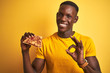 © Krakenimages.com - African american man eating slice of pizza standing over isolated yellow background doing ok sign with fingers, excellent symbol