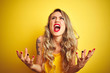 Young beautiful woman wearing t-shirt standing over yellow isolated background crazy and mad shouting and yelling with aggressive expression and arms raised. Frustration concept.