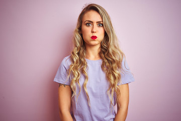 Sticker - Young beautiful woman wearing purple t-shirt standing over pink isolated background puffing cheeks with funny face. Mouth inflated with air, crazy expression.